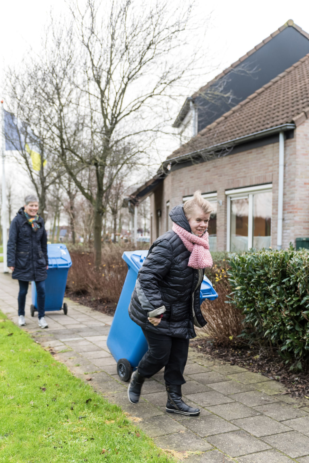 Vrouw zet een blauwe kliko aan de straat bij Visio in Emmen