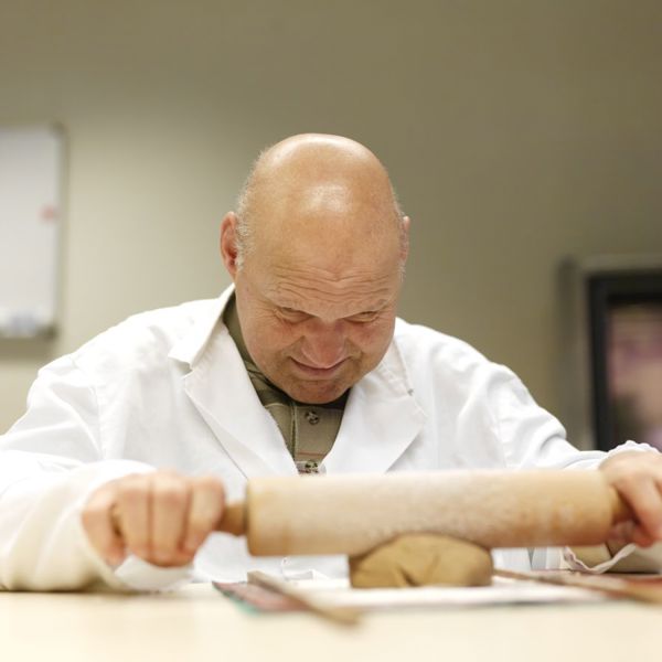 Man met een visuele en verstandelijke beperking rolt deeg uit Man met een visuele en verstandelijke beperking rolt deeg uit