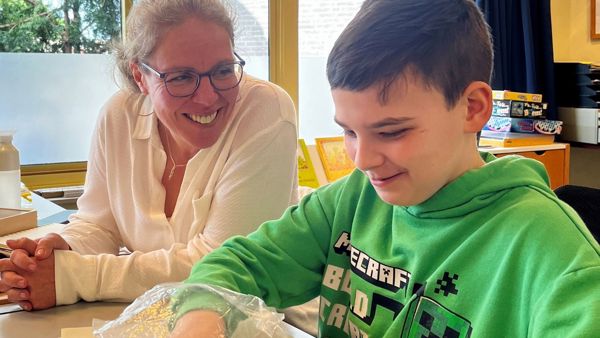Dean met ambulant onderwijskundig begeleider van Visio aan tafel in een klaslokaal Dean met ambulant onderwijskundig begeleider van Visio aan tafel in een klaslokaal