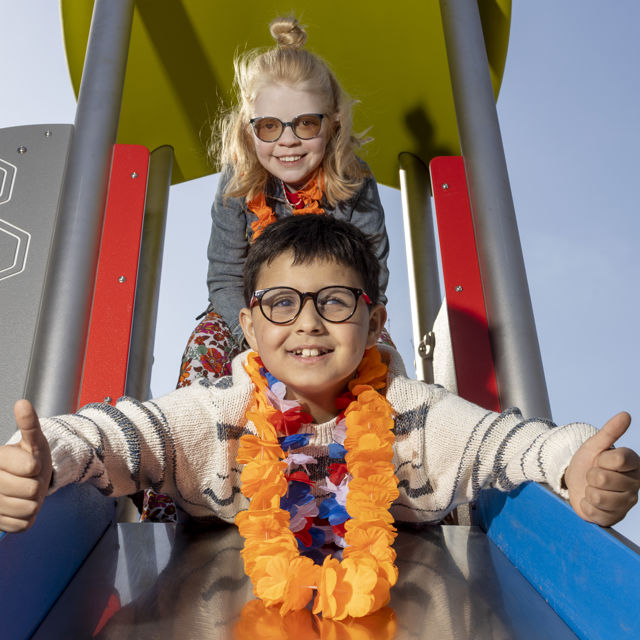 Twee kinderen, een jongen en een meisje, gaan samen van de glijbaan af. De jongen steekt zijn duimen omhoog. Twee kinderen, een jongen en een meisje, gaan samen van de glijbaan af. De jongen steekt zijn duimen omhoog.