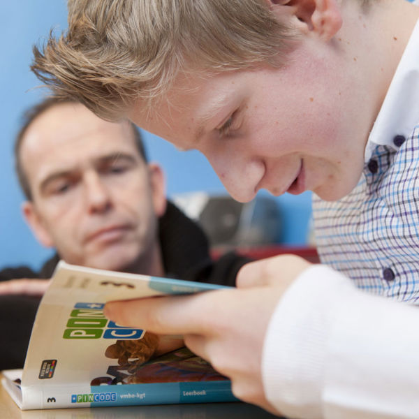 Leerling kijkt in een boek terwijl een docent meekijkt. Leerling kijkt in een boek terwijl een docent meekijkt.