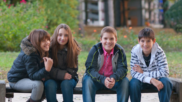 Vier kinderen, twee jongens en twee meisjes, zitten samen op een bankje. Ze kijken lachend naar de camera. Vier kinderen, twee jongens en twee meisjes, zitten samen op een bankje. Ze kijken lachend naar de camera.