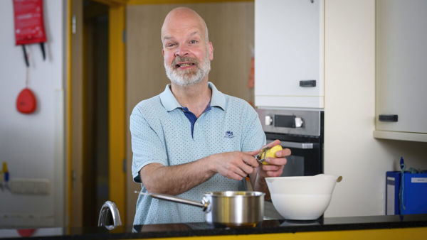 Man schilt aardappels in een keuken op een Visio-locatie en glimlacht daarbij Man schilt aardappels in een keuken op een Visio-locatie en glimlacht daarbij