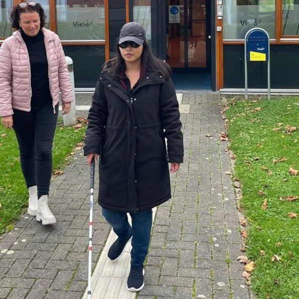 visio-het-loo-erf-Athittiya-Auaychai-loopt-met-stok-begeleid-door-medewerkerk.jpg visio-het-loo-erf-Athittiya-Auaychai-loopt-met-stok-begeleid-door-medewerkerk.jpg