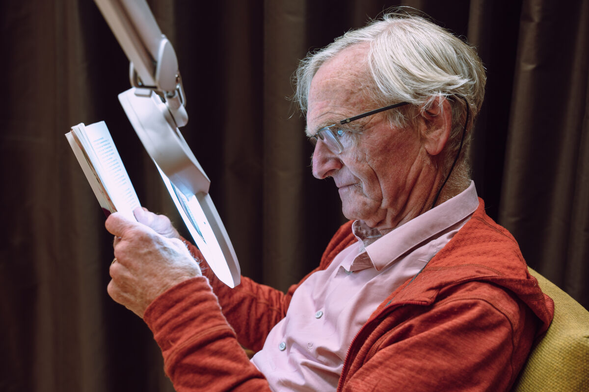 Man met visuele beperking leest met speciale leeslamp