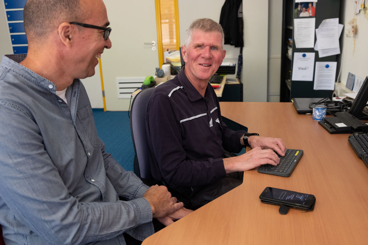 Cliënt krijgt training bij Visio Het Loo Erf en zit daarbij aan een bureau waarbij hij een brailletoetsenbord gebruikt