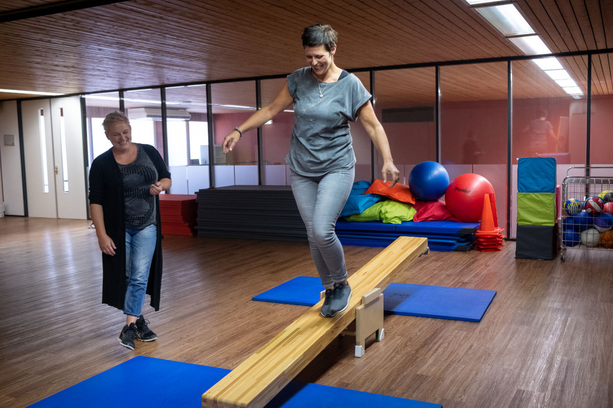 Cliënt van Visio Het Loo Erf voert bewegingsoefeningen uit in een sportzaal onder begeleiding van een medewerker