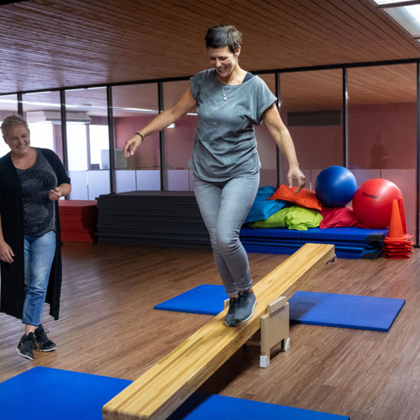 Cliënt van Visio Het Loo Erf voert bewegingsoefeningen uit in een sportzaal onder begeleiding van een medewerker Cliënt van Visio Het Loo Erf voert bewegingsoefeningen uit in een sportzaal onder begeleiding van een medewerker