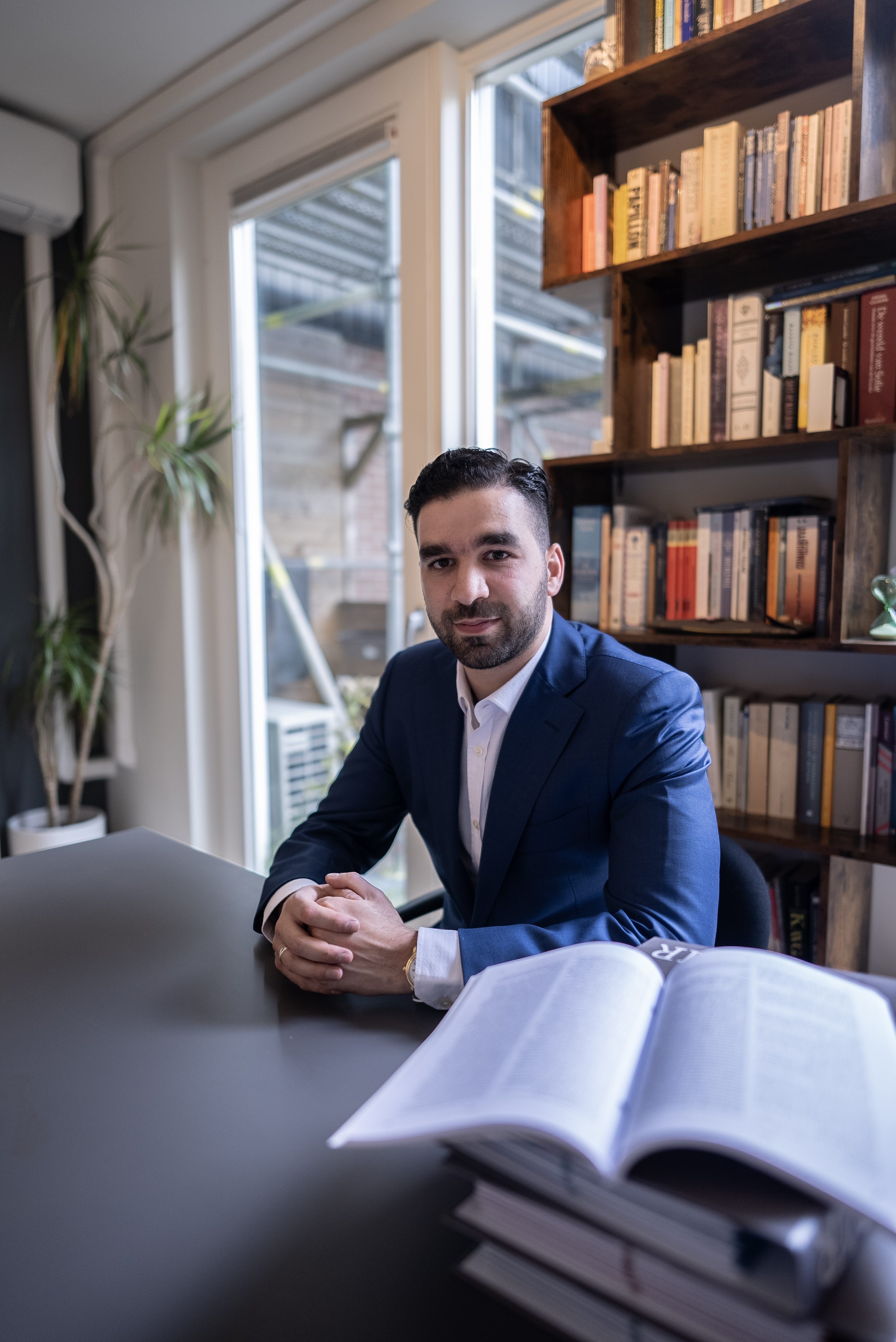 Foto van Faruk, hij zit aan een bureau in een kantoor met een blauw pak aan.