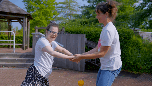 Cliënt met een visuele en verstandelijke beperking en haar begeleider draaien rondjes op een speeltoestel Cliënt met een visuele en verstandelijke beperking en haar begeleider draaien rondjes op een speeltoestel
