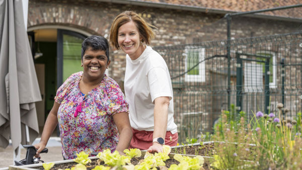 Cliënt en medewerker van Visio poseren glimlachend bij een moestuin Cliënt en medewerker van Visio poseren glimlachend bij een moestuin