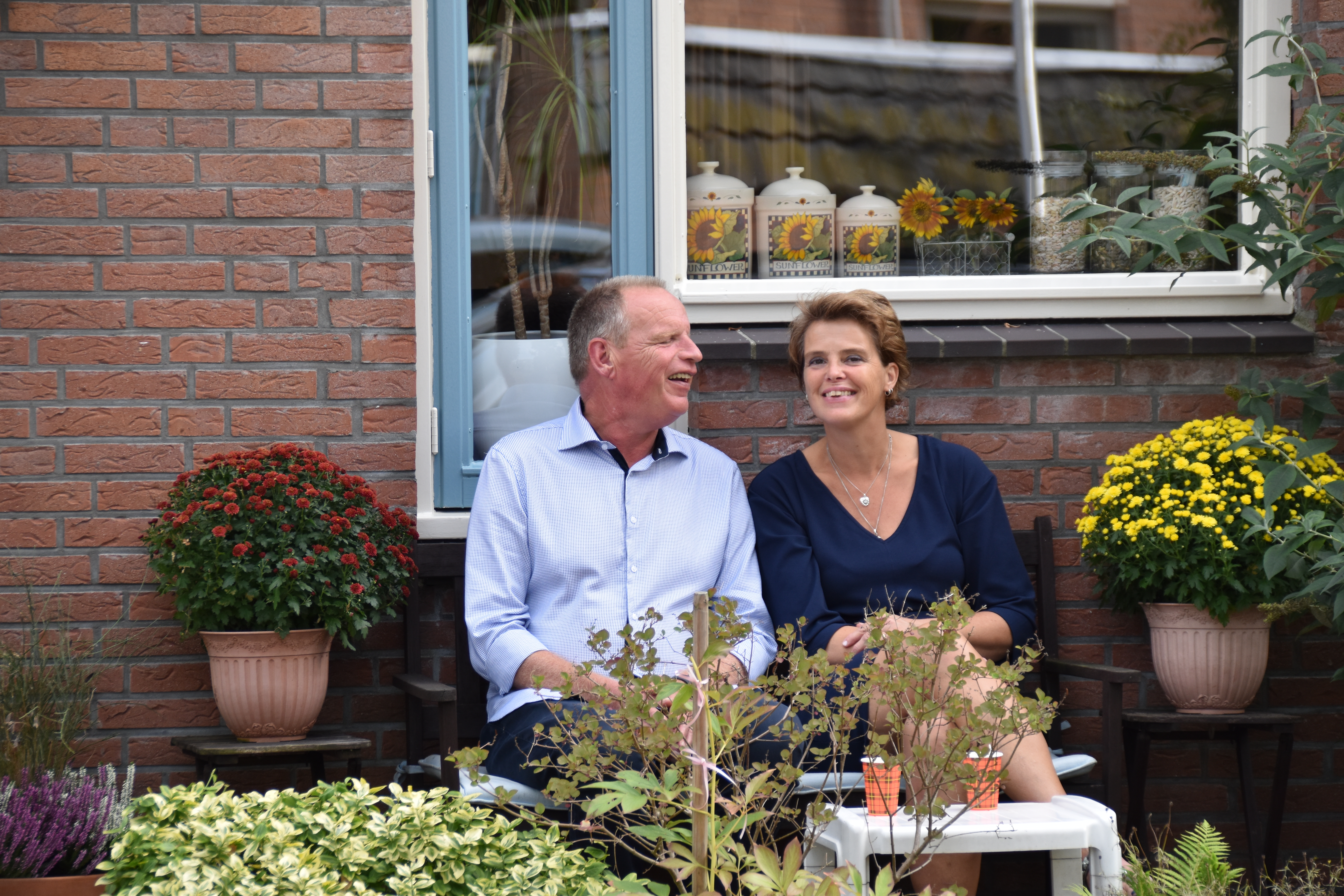 Renate en Jan zitten samen op een bankje in de tuin. Ze zijn omringd door planten. 