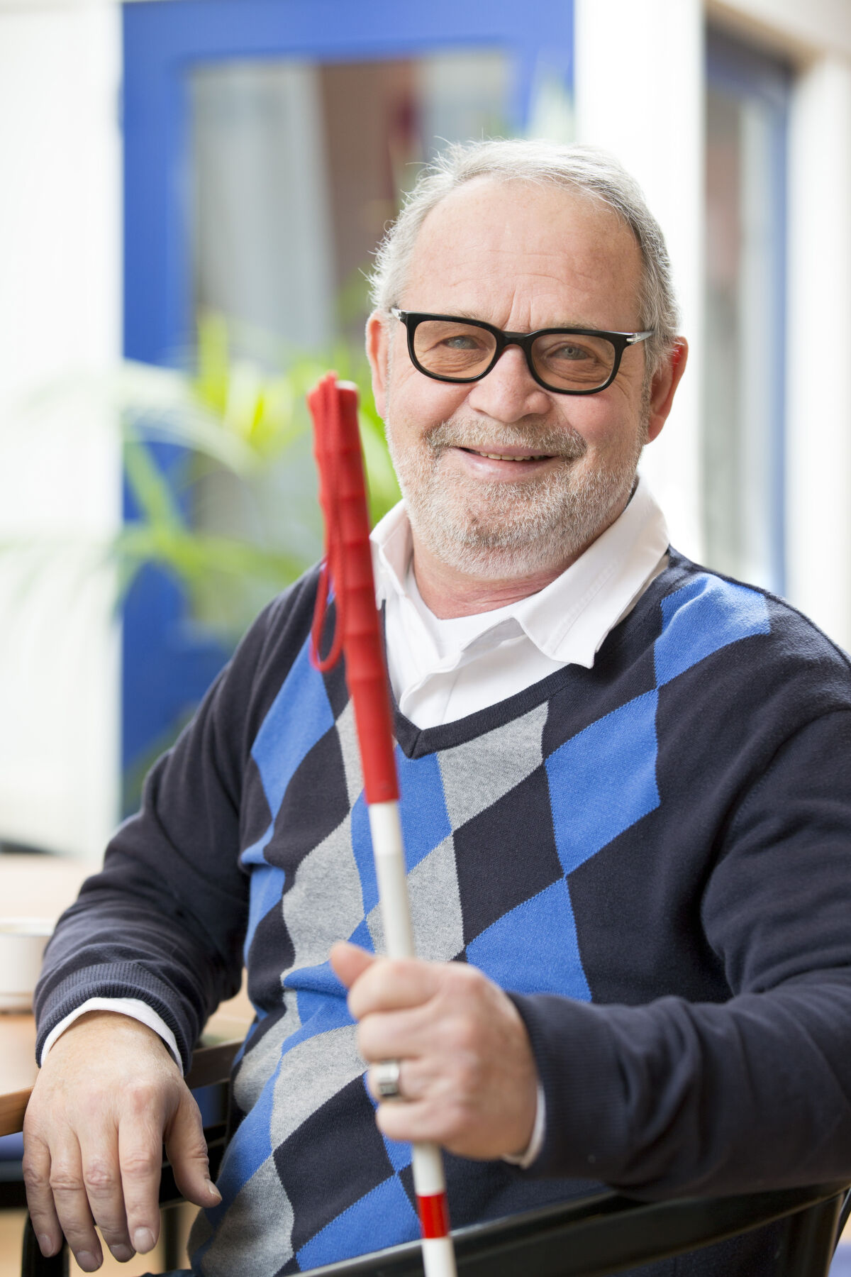 Oudere man met glaucoom glimlacht zittend met een taststok in zijn hand